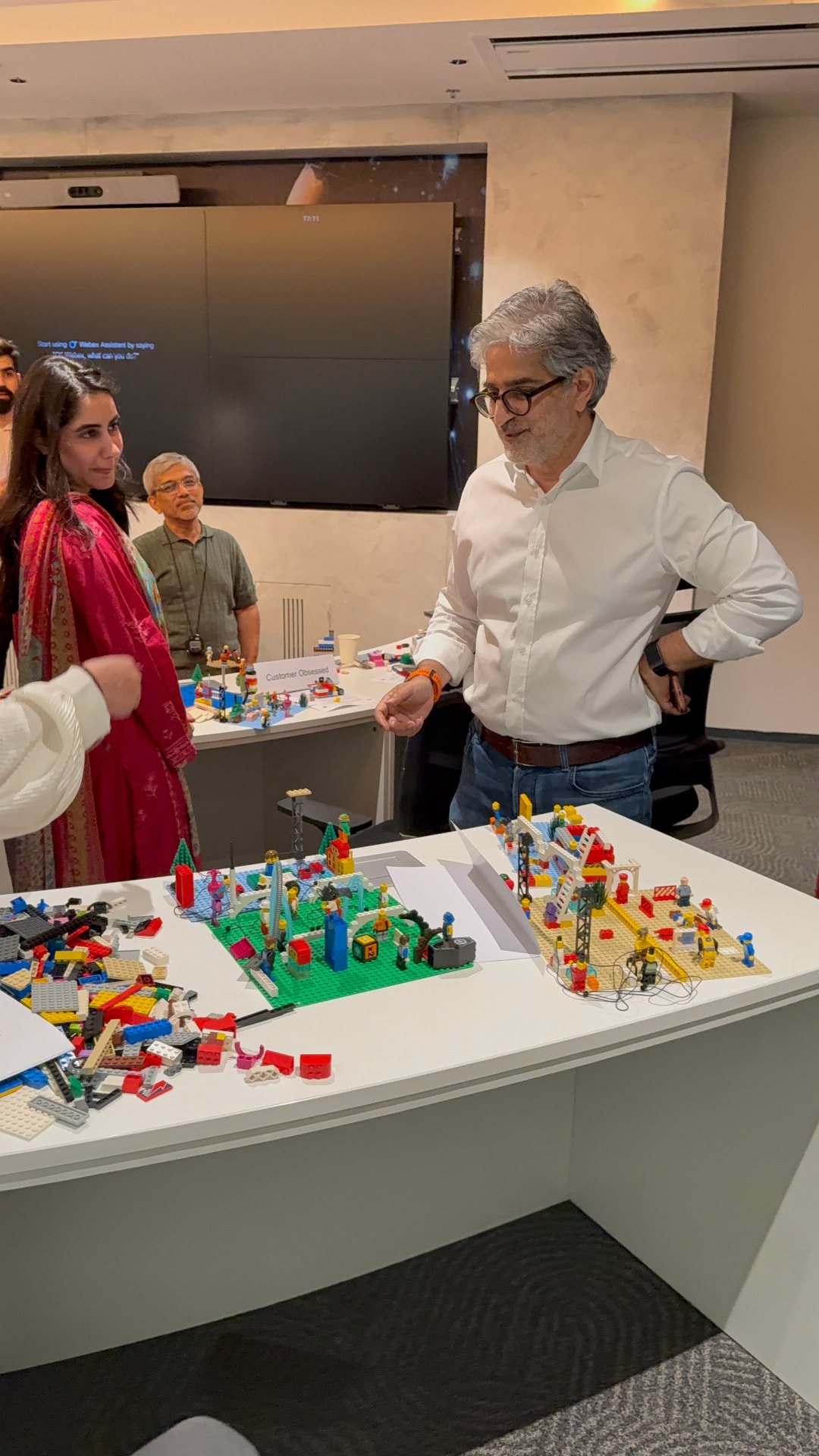 Facilitator in a white shirt guiding Jazz employees around a table of LEGO models during a LEGO AdVentures session at Jazz World HQ